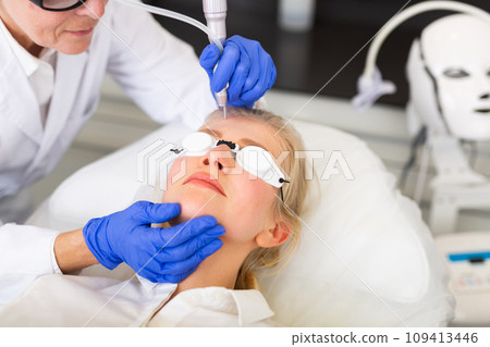 Cosmetologist using laser to resurface skin of young woman's face 109413446