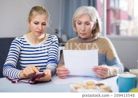 Mature woman and her adult daughter study an important document Mature woman and her adult daughter study an important document 109413548