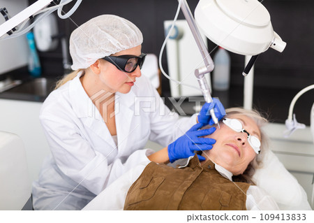 Female cosmetologist performing laser facial treatment to elderly woman 109413833