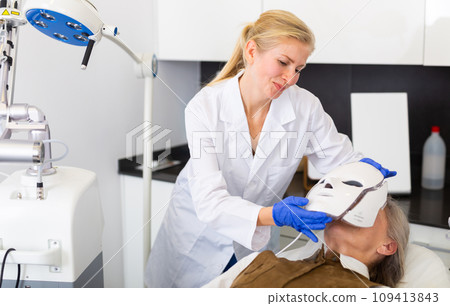 Elderly woman receiving facial light therapy in aesthetic medicine office 109413843