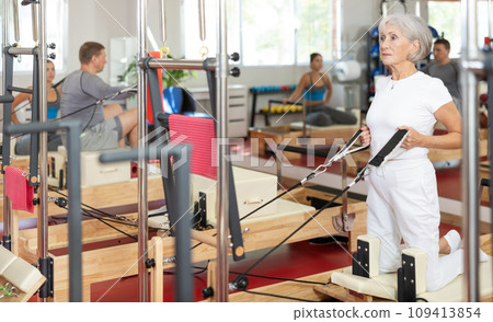 Elderly woman training her arms using straps Elderly woman training her arms using straps 109413854