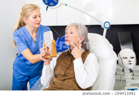 Cosmetologist explaining future facial procedure to elderly female patient 109413981