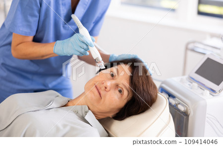 Aged woman undergoing cosmetic facial treatment using ion bubble attachment Aged woman undergoing cosmetic facial treatment using ion bubble attachment 109414046