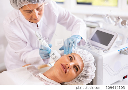 Young woman undergoing hardware facial treatment using cold hammer Young woman undergoing hardware facial treatment using cold hammer 109414103