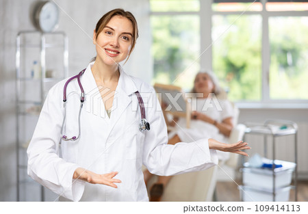 Smiling senior woman doctor in uniform with woman patient lying behind in clinic. Smiling senior woman doctor in uniform with woman patient lying behind in clinic. 109414113