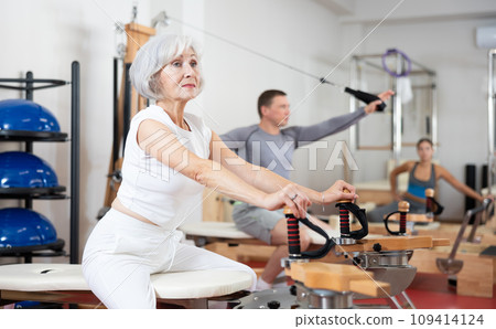 Mature woman during Pilates training performs exercises and tasks on heron pulley tower Mature woman during Pilates training performs exercises and tasks on heron pulley tower 109414124