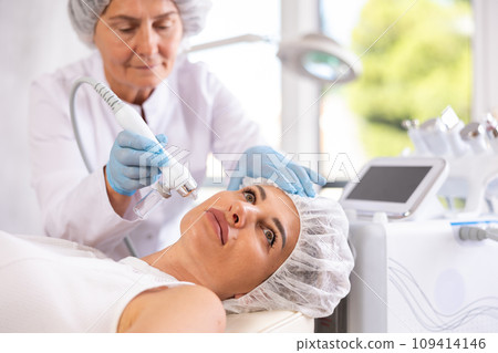 Young woman undergoing facial skin therapy using airbrush wuth atomized nutrients 109414146