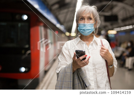 Senior woman in face mask with phone waiting for subway train 109414159