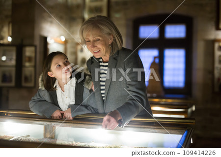 Aged female tutor with preteen girl exploring showpieces in museum 109414226