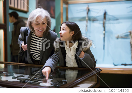 Preteen girl with grandmother viewing ancient handguns in museum 109414303