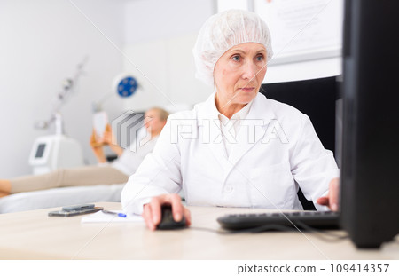 Elderly female cosmetologist working with laptop in aesthetic medicine office 109414357