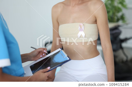 Doctor mammologist holds xray in clipboard near patient with bandaged chest in clinic closeup 109415284