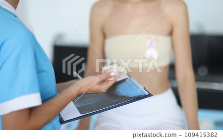 Doctor's hands are holding breast implant in front of clipboard with patient in background Doctor's hands are holding breast implant in front of clipboard with patient in background 109415382