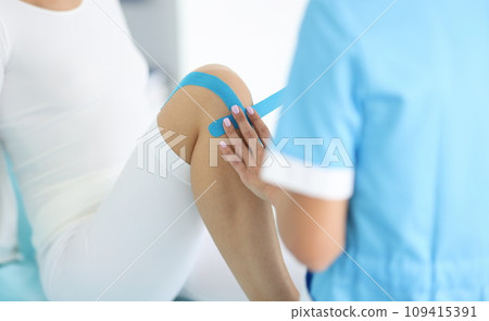 Traumatologist conducts taping of patient's leg in hospital closeup Traumatologist conducts taping of patient's leg in hospital closeup 109415391