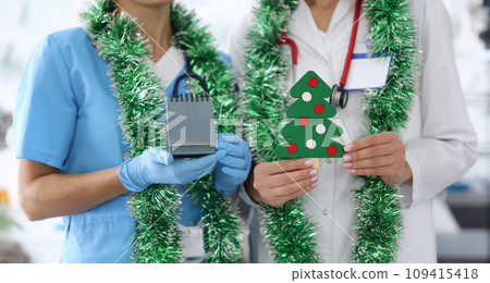 Nurse with white coat hold paper Christmas tree with decorations. 109415418