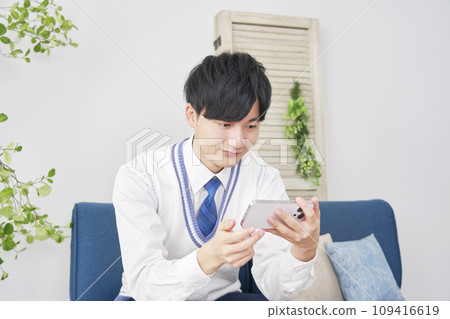 High school boy watching videos on smartphone in living room 109416619