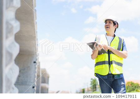 Asian professional - senior cilvil or construction engineer inspecting a segmenting bridge blueprint and construction plan at the site, civil engineer working at bridge construction site. Asian professional - senior cilvil or construction engineer inspecting a segmenting bridge blueprint and construction plan at the site, civil engineer working at bridge construction site. 109417011
