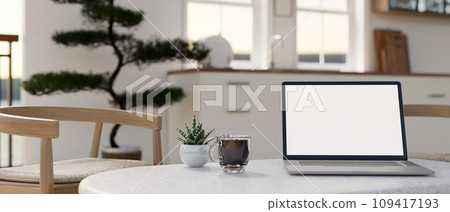 Home workspace, a white-screen laptop mockup on a white coffee table in a minimalist white kitchen. Home workspace, a white-screen laptop mockup on a white coffee table in a minimalist white kitchen. 109417193