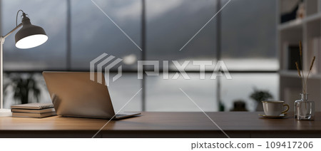 A laptop computer, a table lamp, and decor on a wooden desk in a modern, luxury CEO office room. A laptop computer, a table lamp, and decor on a wooden desk in a modern, luxury CEO office room. 109417206
