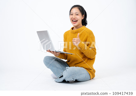 Happy woman sits on the floor on an isolated white background with her laptop and showing thumb up. 109417439