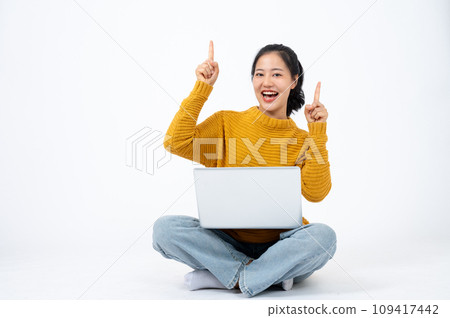 Beautiful woman sits on an isolated white background with her laptop and pointing her finger up. Beautiful woman sits on an isolated white background with her laptop and pointing her finger up. 109417442