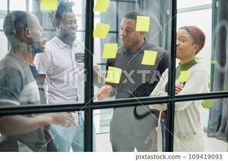 a team of young designers sticking notes on glass in a modern office a team of young designers sticking notes on glass in a modern office 109419093