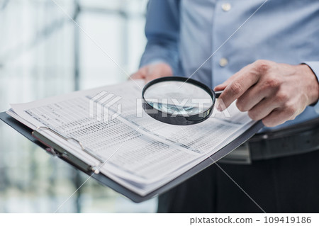 Businessman looking through a magnifying glass to documents Businessman looking through a magnifying glass to documents 109419186