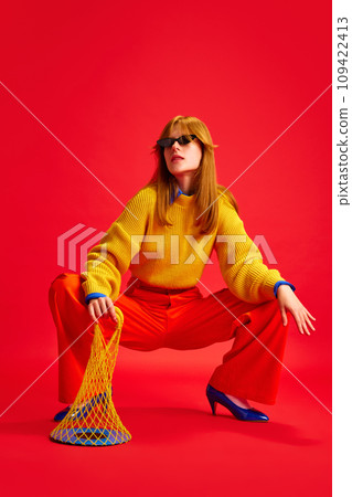 Cool attractive girl sitting posing dressed retro casual outfit in eyewear and holds transparent bag with plate against vivid red background. 109422413