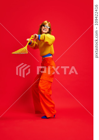 Creative portrait of funny girl, dancing dressed bright retro fashion outfit with sunglasses, accessories against vivid red background. 109422416