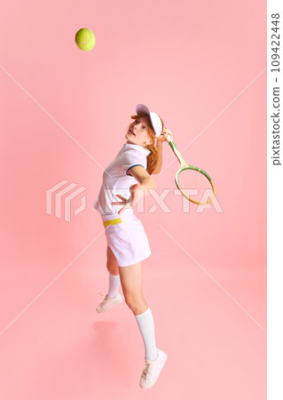 Top. view. Full-length portrait of confident, beautiful woman, tennis player hitting tennis ball with racket in motion against pastel pink background Top. view. Full-length portrait of confident, beautiful woman, tennis player hitting tennis ball with racket in motion against pastel pink background 109422448