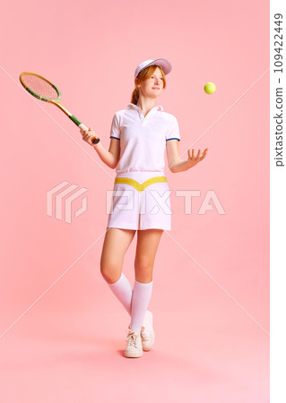 Full-length portrait of confident, beautiful woman, tennis player tosses ball with one hand against pastel pink background Full-length portrait of confident, beautiful woman, tennis player tosses ball with one hand against pastel pink background 109422449