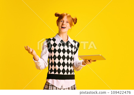 Portrait of adorable, pleasantly surprised girl, student holding tablet against yellow background. Concept of online shopping. Portrait of adorable, pleasantly surprised girl, student holding tablet against yellow background. Concept of online shopping. 109422476