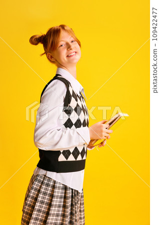 Side view portrait of adorable, cheerful smiling girl, student holds new just bought book against yellow background. Side view portrait of adorable, cheerful smiling girl, student holds new just bought book against yellow background. 109422477