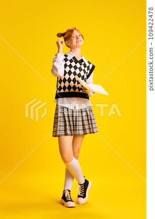 Faull-length portrait of adorable red haired girl, dressed retro fashion outfit reading book against yellow background. Concept of education. Faull-length portrait of adorable red haired girl, dressed retro fashion outfit reading book against yellow background. Concept of education. 109422478