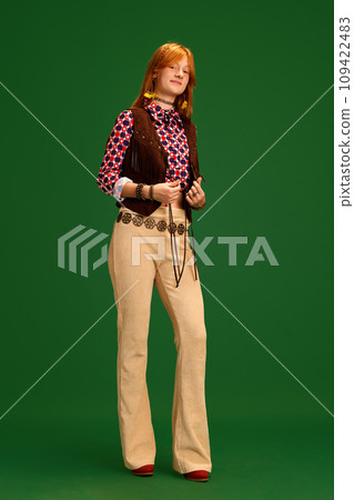 Adorable female fashion model with red hair dressed old-fashioned western style outfit posing against green studio background. 109422483