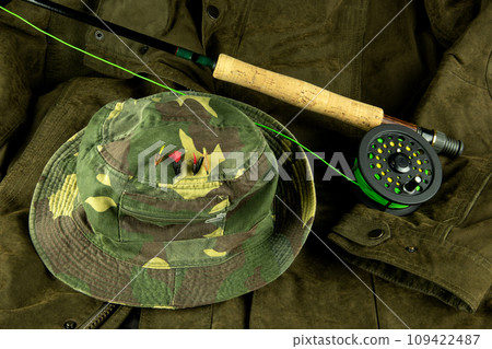 Fly Fishing Rod and Reel with Line on an Outdoor Coat with Fishing Hat and Trout Flies 109422487