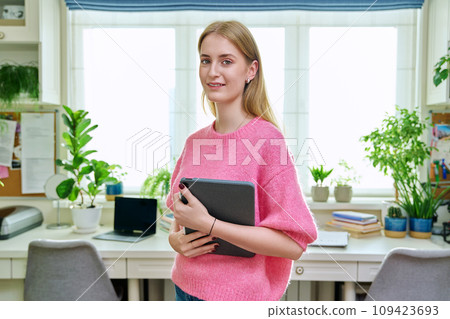 Portrait of teenage girl holding digital tablet looking at camera in room at home Portrait of teenage girl holding digital tablet looking at camera in room at home 109423693