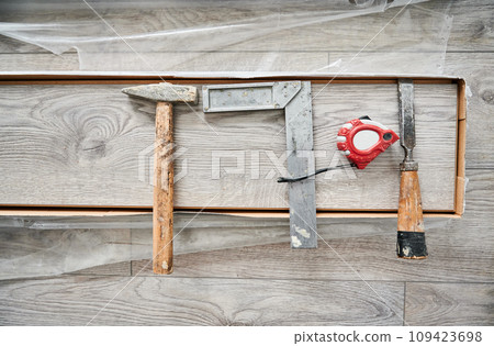 Metal construction ruler, hammer and measuring tape on laminate wood plank. Building repair tools and instruments for laminate flooring installation, construction works and home renovation. Metal construction ruler, hammer and measuring tape on laminate wood plank. Building repair tools and instruments for laminate flooring installation, construction works and home renovation. 109423698