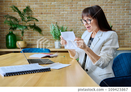 Mature business woman reading an important letter, rejoicing at good news Mature business woman reading an important letter, rejoicing at good news 109423867