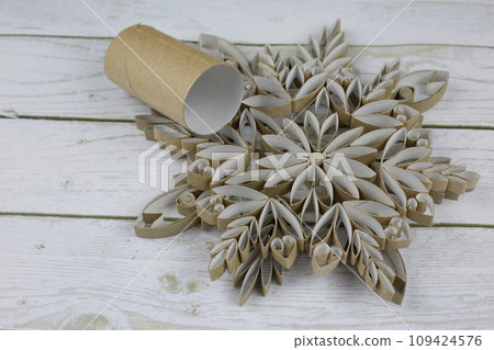 Craft a snowflake from toilet paper rolls. New Year's homemade toys from scrap materials. Home holiday decorations made from recycled materials on white wooden background 109424576