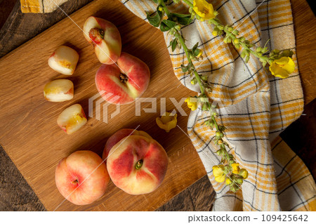 Cutting board with cut and whole saturn peaches or flat peaches on wooden background with yellow kitchen towel.. Cutting board with cut and whole saturn peaches or flat peaches on wooden background with yellow kitchen towel.. 109425642