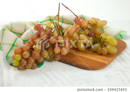 Cutting board with bunch of organic pink grapes on white wooden background.. Cutting board with bunch of organic pink grapes on white wooden background.. 109425843