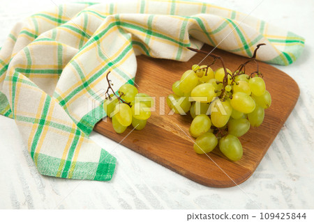 Cutting board with bunch of organic green grapes on white wooden background.. Cutting board with bunch of organic green grapes on white wooden background.. 109425844