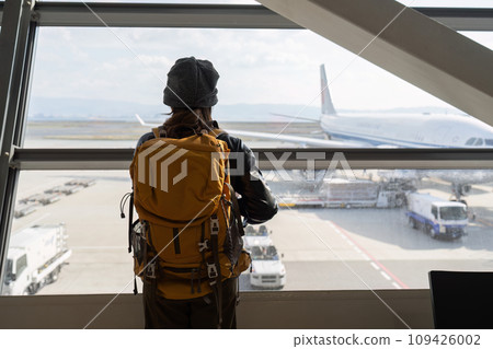 Traveler woman plan and backpack see airplane flight at the airport glass window Traveler woman plan and backpack see airplane flight at the airport glass window 109426002
