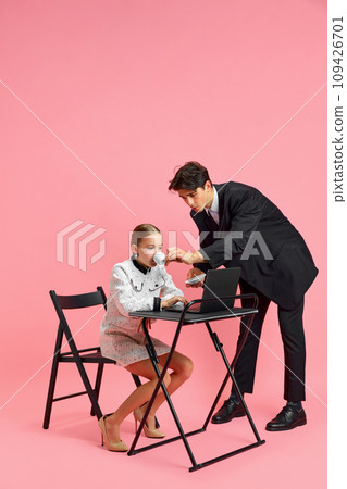 Secretary drinks tea for her little executive, entrepreneur who sits at desk with laptop and works hard against pink studio background. 109426701
