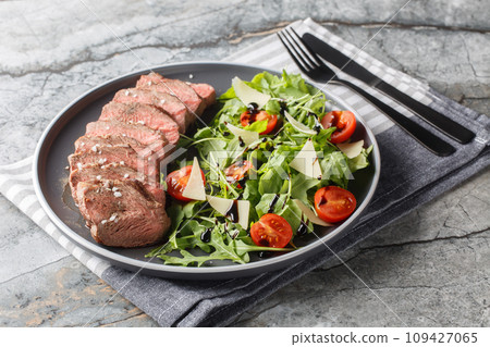 Beef steak tagliata with arugula, parmesan,  cherry tomatoes and balsamic close-up on a plate. Horizontal 109427065