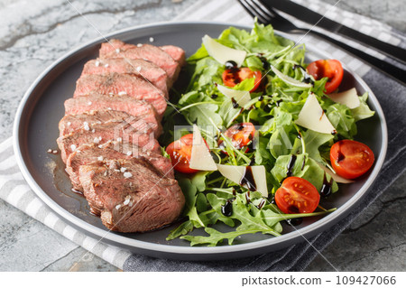 Traditional Italian main dish Beef tagliata tender steak, arugula, cherry tomatoes, Grana Padano shavings, balsamic reduction close-up on a plate on the table. Horizontal 109427066