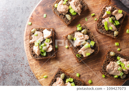 Tasty sandwiches with cod liver, capers and green onion close-up on a wooden board. Horizontal top view Tasty sandwiches with cod liver, capers and green onion close-up on a wooden board. Horizontal top view 109427073