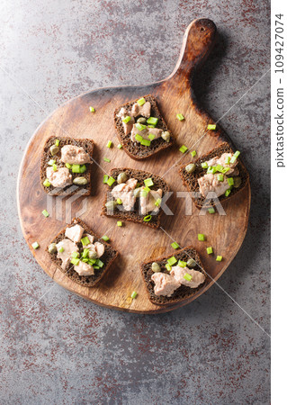 Sandwiches with canned cod liver, green onions and capers close-up on a wooden board. Vertical top view Sandwiches with canned cod liver, green onions and capers close-up on a wooden board. Vertical top view 109427074