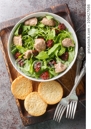Healthy food cod liver salad with mixed leafy greens and sun-dried tomatoes close-up in a bowl. Vertical top view Healthy food cod liver salad with mixed leafy greens and sun-dried tomatoes close-up in a bowl. Vertical top view 109427086